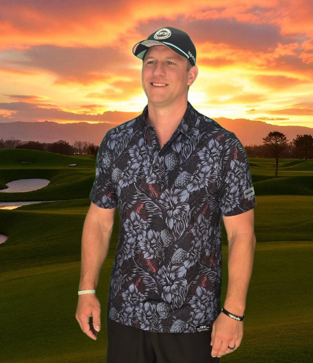 Man in a dark blooms golf polo shirt and cap standing on a golf course with a sunset in the background
