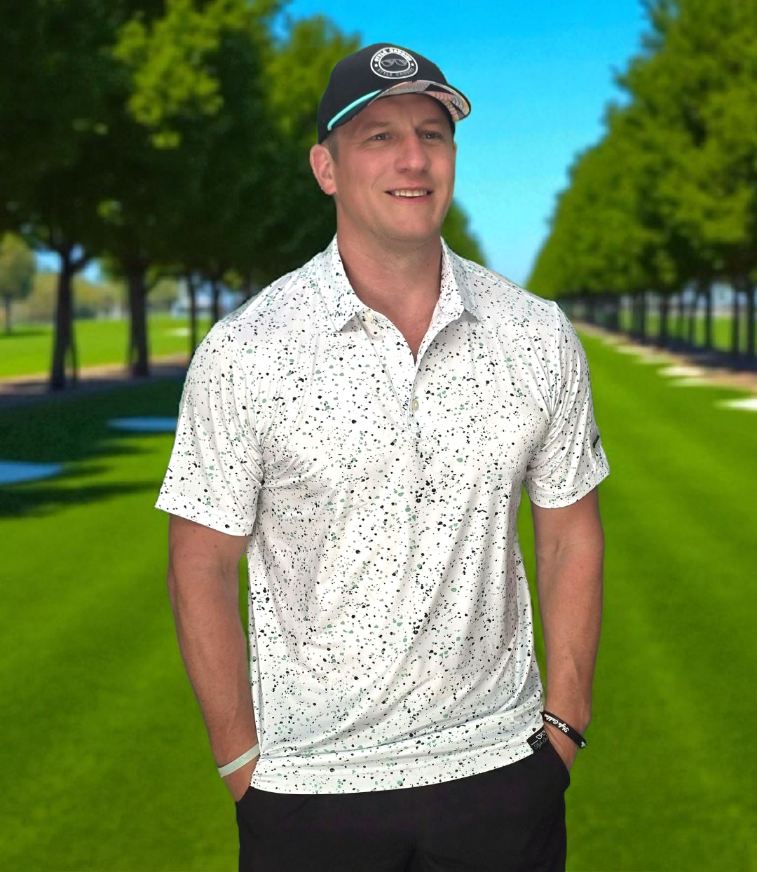Man wearing a splattered golf polo shirt and black cap standing on a golf course.