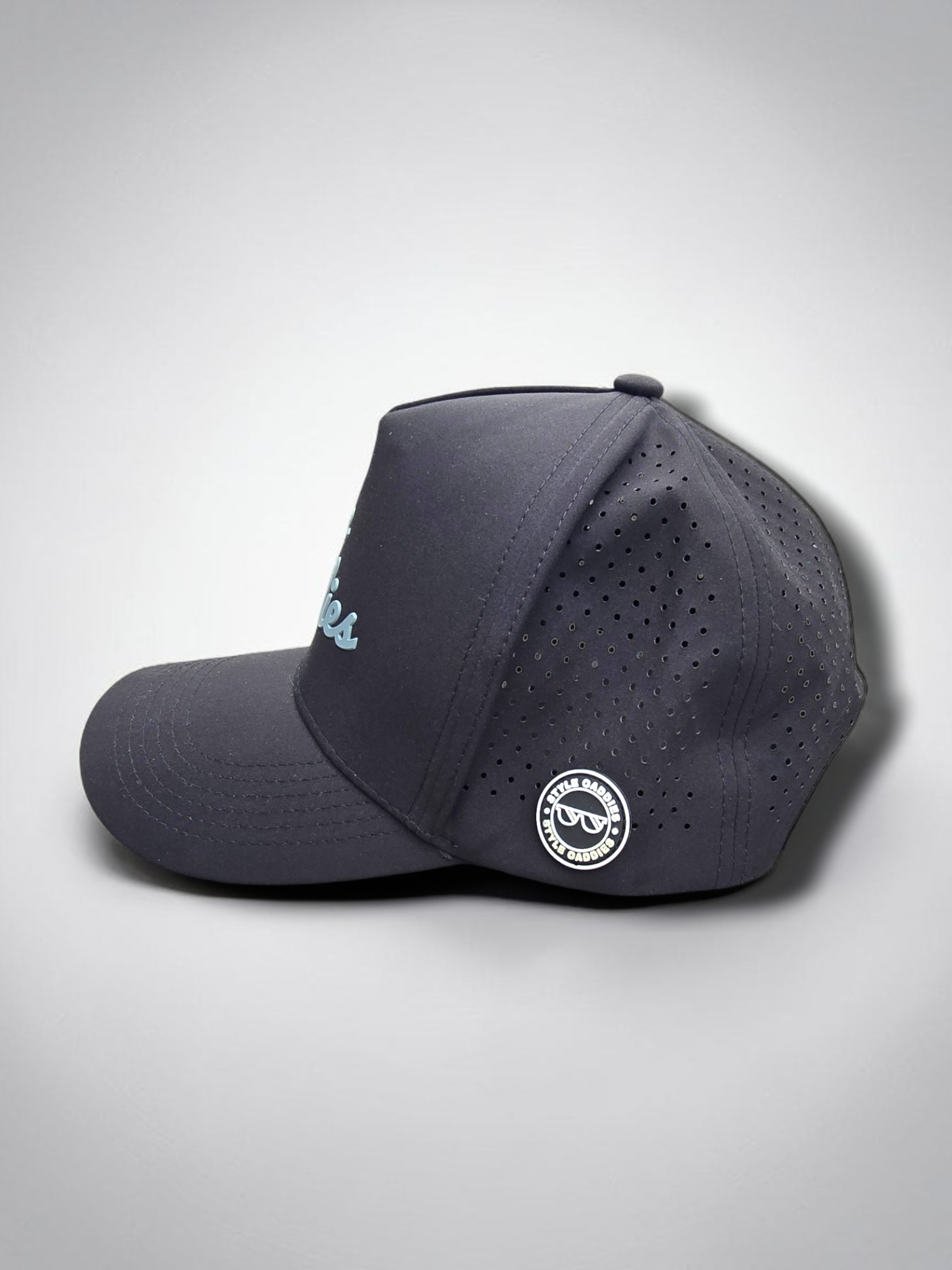 Black Style Caddies hat side profile close-up showing the perforated panel and circular logo patch